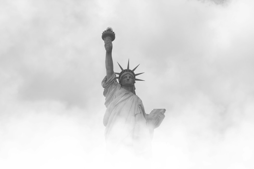A picture of the statue of liberty that appears to be in grayscale. She is half concealed in fog and clouds.